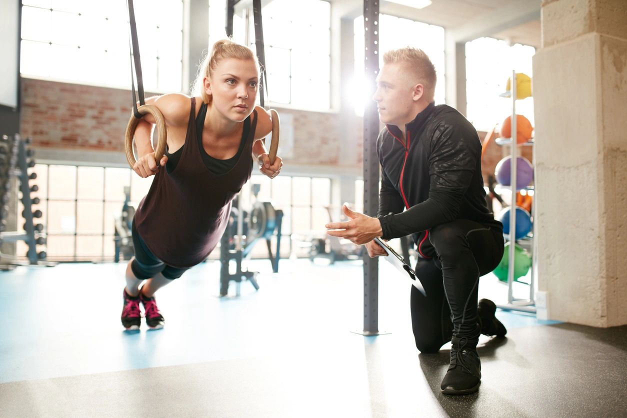 Woman training with coach using gym rings.